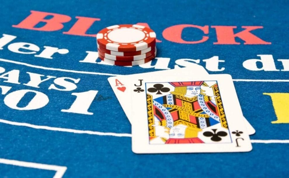 A blackjack hand and four casino chips on top of a blue blackjack table.
