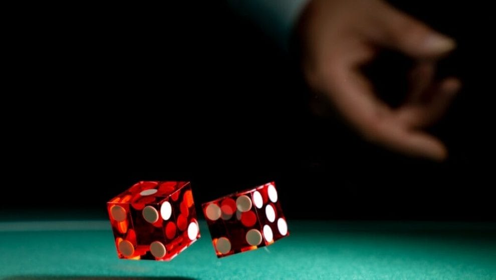 A person throws two red dice onto the felt of a poker table.