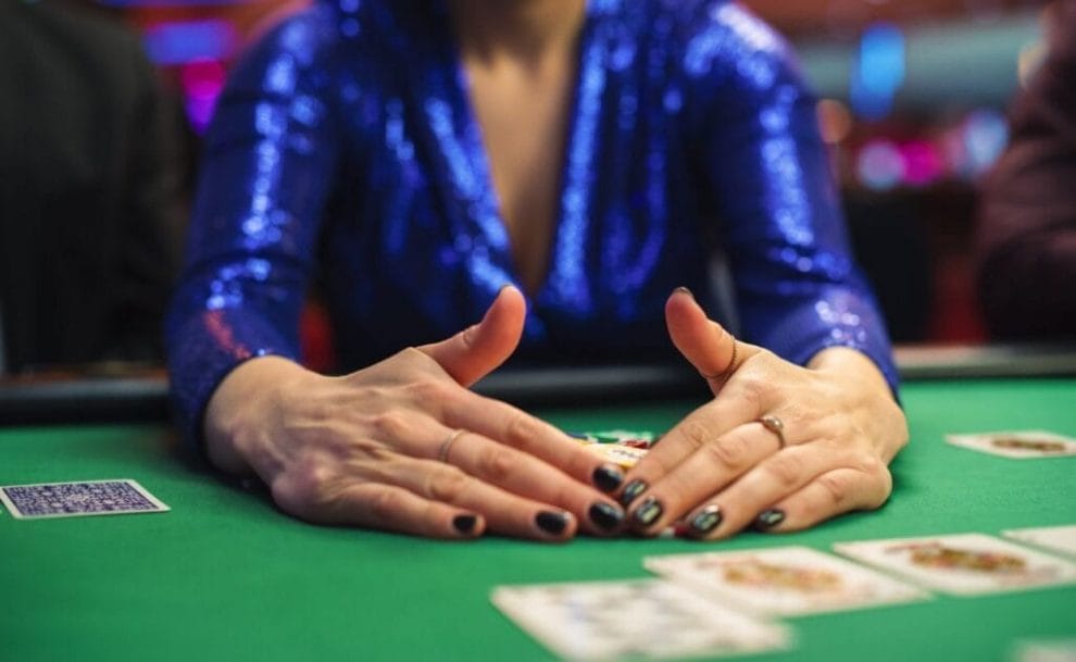 A person seated at a poker table, collecting poker chips with both hands.