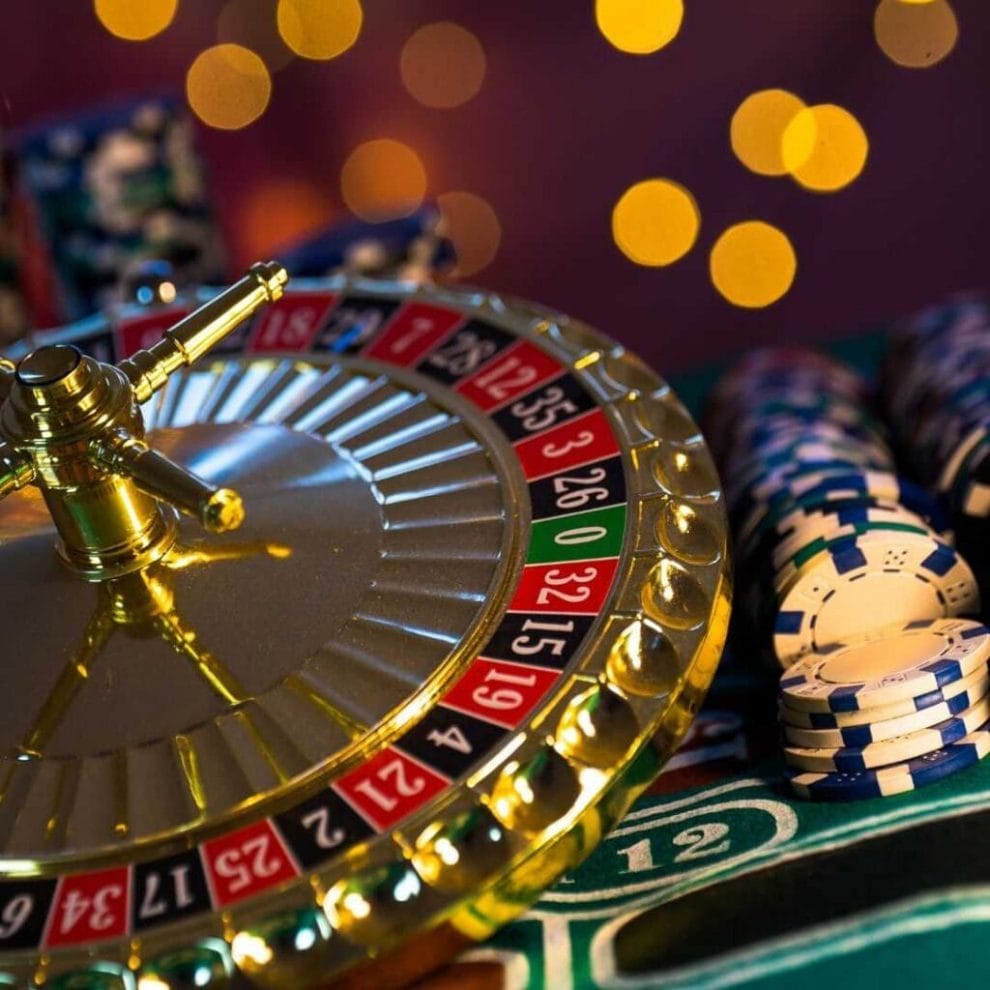 A gold roulette wheel balancing on top of casino chips on top of a roulette table.