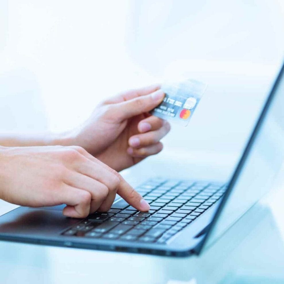 A person entering card details onto a laptop with a card in their hand.