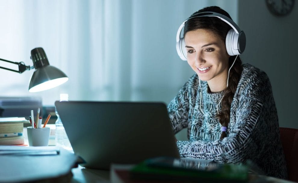 A person wearing headphones and smiling while using their laptop.