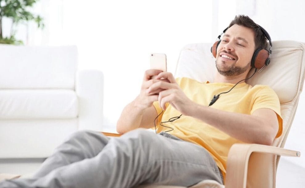 A person lying back in a recliner while wearing headphones and using their smartphone.
