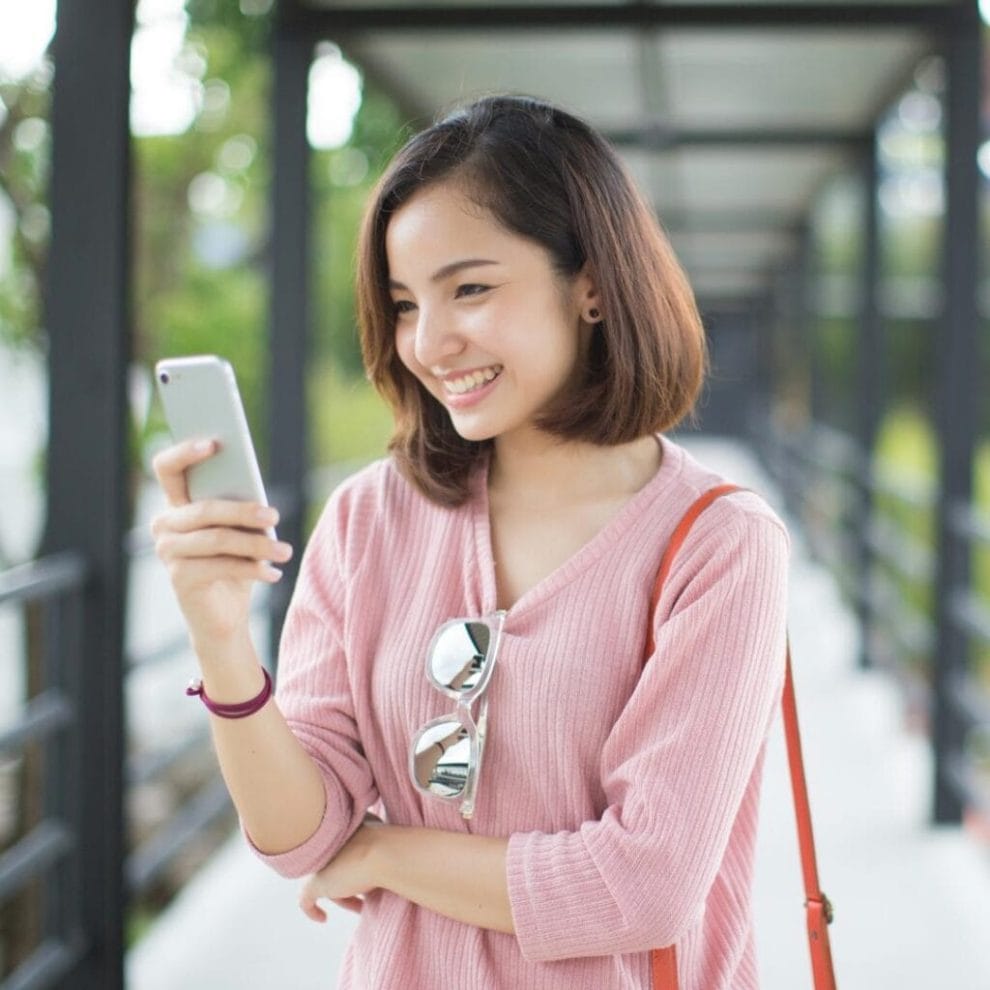 A person smiling while looking at their cell phone outdoors.