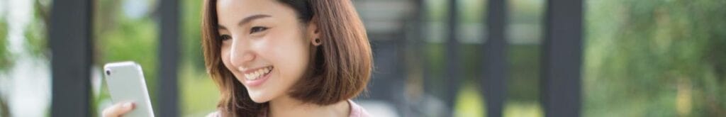 A person smiling while looking at their cell phone outdoors.