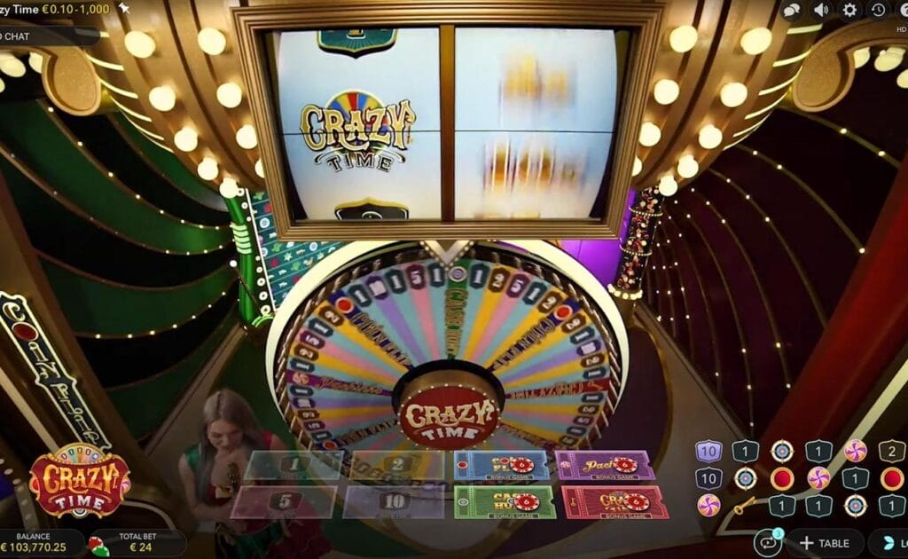 The gameplay in Crazy Time from the Evolution promotional video. The camera is focused on the top slot as it spins, with the wheel spinning below it. The host stands on the left side next to the wheel.