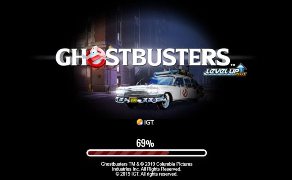 A screenshot of the Ghostbusters Plus loading screen showing the game’s logo and the Ectomobile lit up by a spotlight on a black background. 