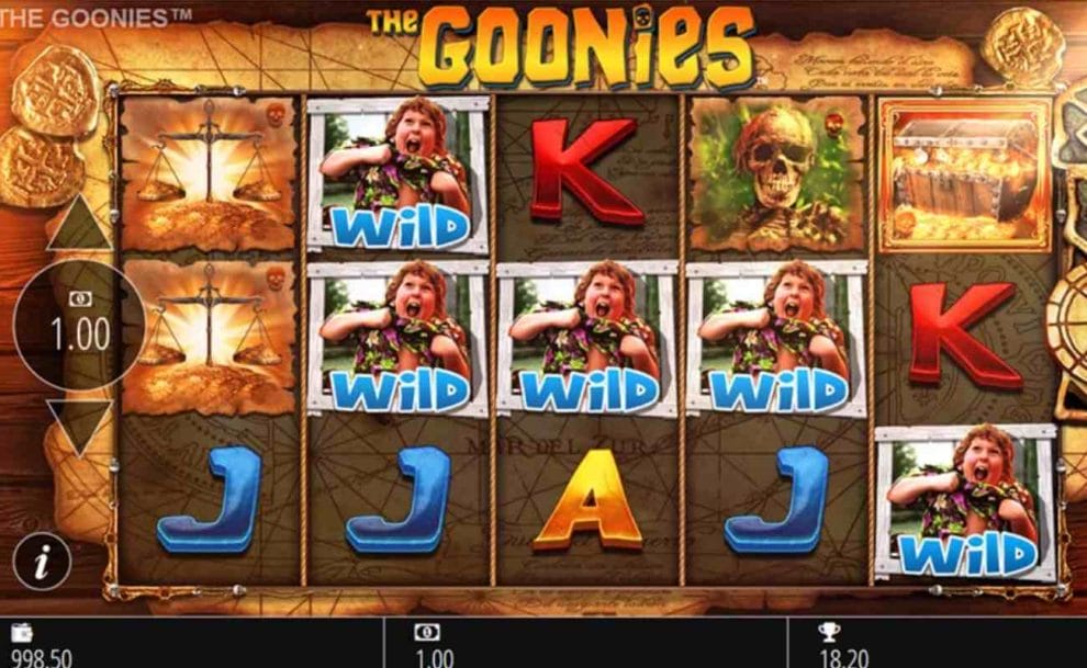 A screenshot of the slot reels of The Goonies online slot game showing a few low-paying card royal symbols, several Wild symbols, balance scale symbols, a skeleton, and a golden chest.