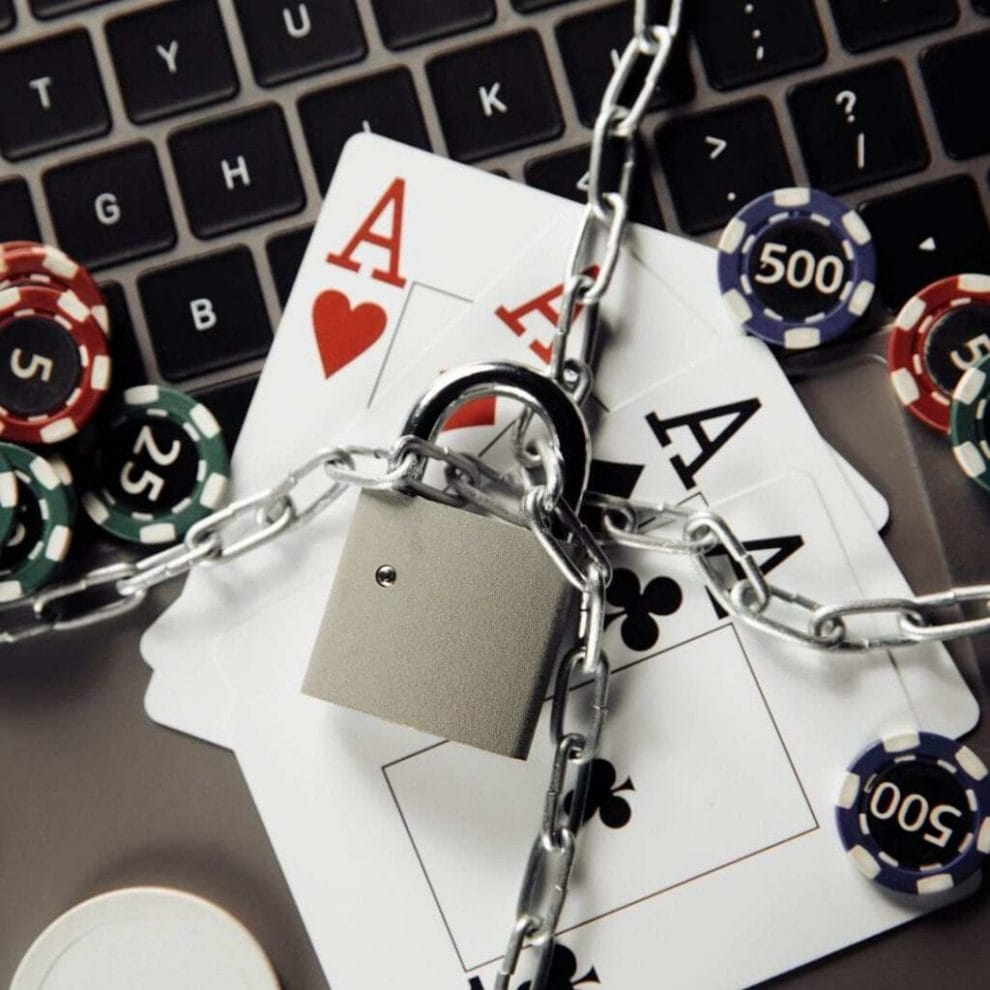 A responsible gambling concept image of a laptop, poker chops, and four Ace playing cards with chains and a lock around them.