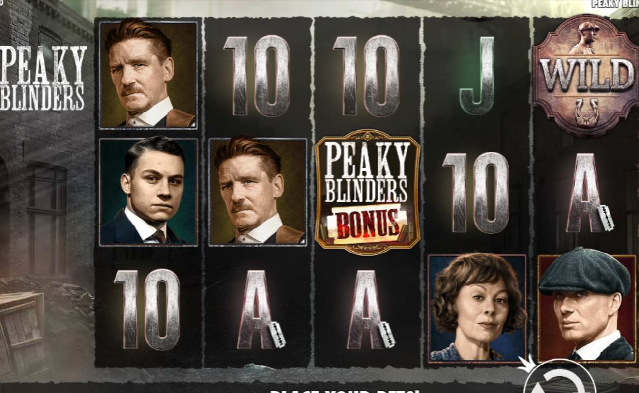 Peaky Blinders online slot with silver playing card symbols and Peaky Blinder characters against black reels. The background shows a street and a building in Birmingham.