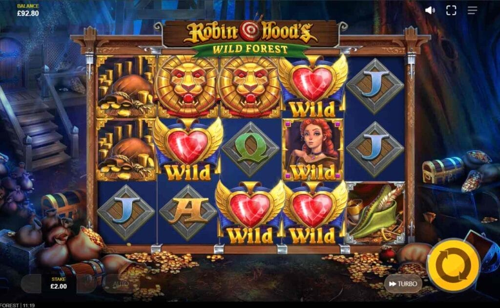 Robin Hood’s Wild Forest online slot with gold lion symbols, playing cards J and A, and wild gold heart symbols against a metal diamond frame. The yellow spin button is against a dark background with tree roots and gold coins.