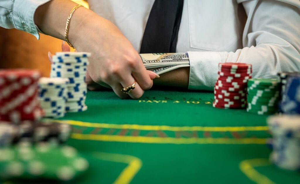 Close-up of hands removing cash from under a sleeve with a green felt table and casino chips.