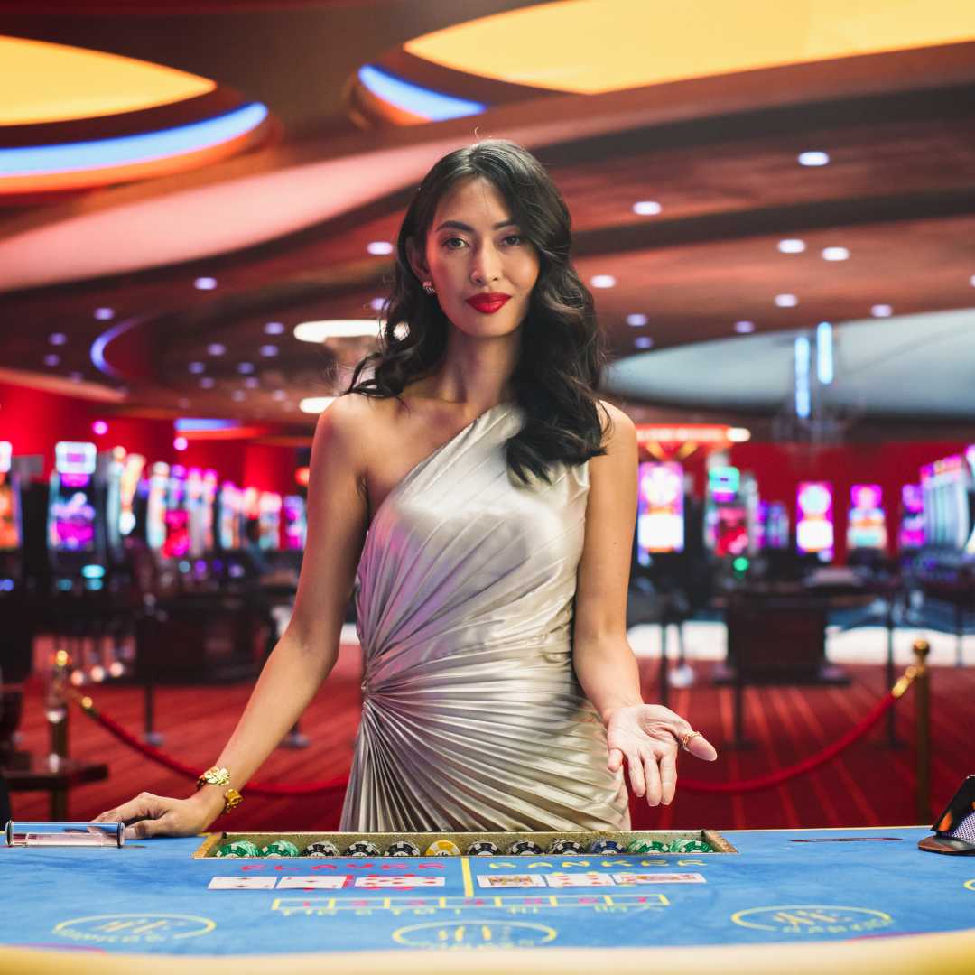 Portrait of a professional baccarat dealer with an open palm in front of a blue baccarat table.