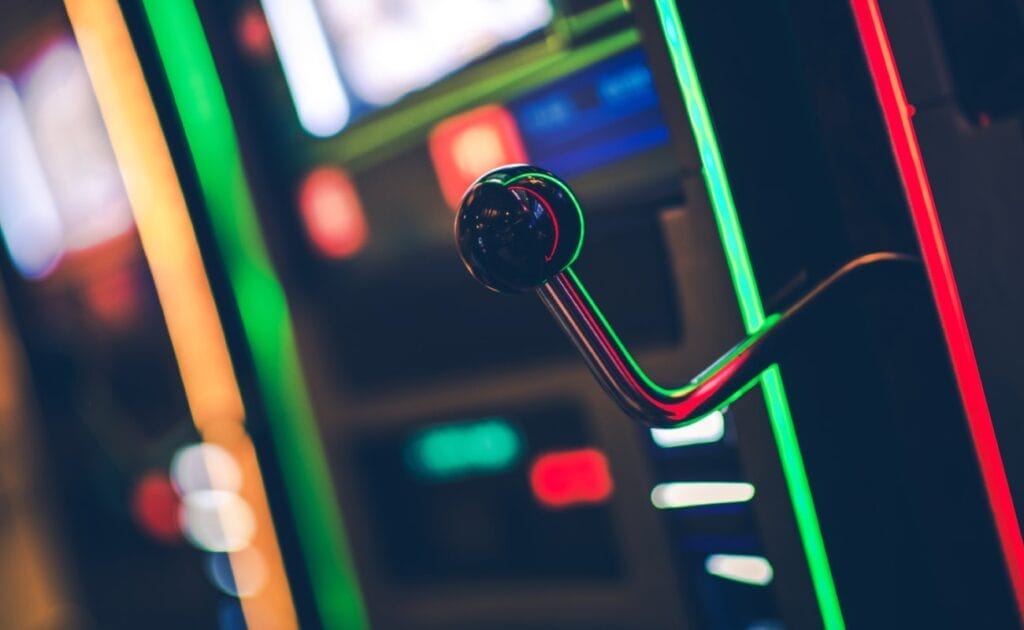 A close-up on a slot machine handle with green, yellow, and red neon lights in the background. 