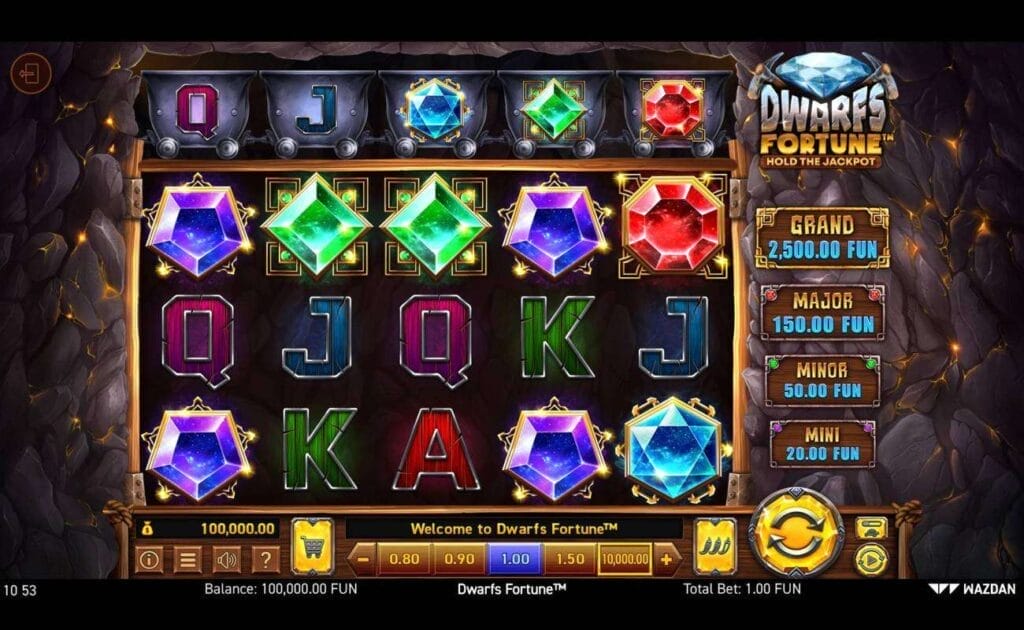 A screenshot of the reels in Dwarfs Fortune. The game is set against a rock wall with glowing gold veins. The reel has a variety of symbols, including different shaped and colored gems, as well as standard slot symbols like the A, K, Q, and J. Above the reels is a row of mining carts. These mining carts have slot symbols on their sides.