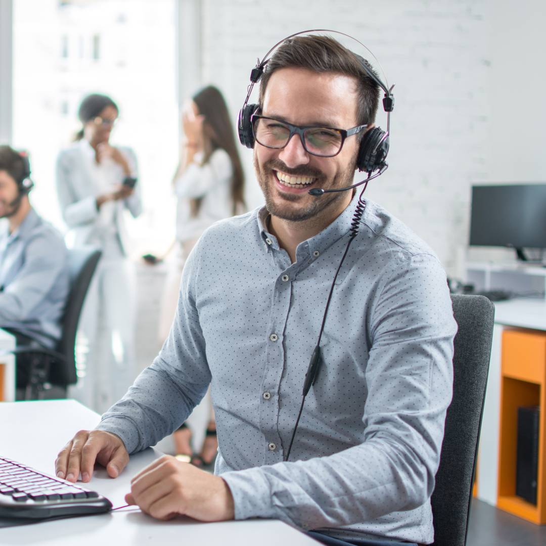 A smiling customer support agent sitting at his desk in front of his computer.