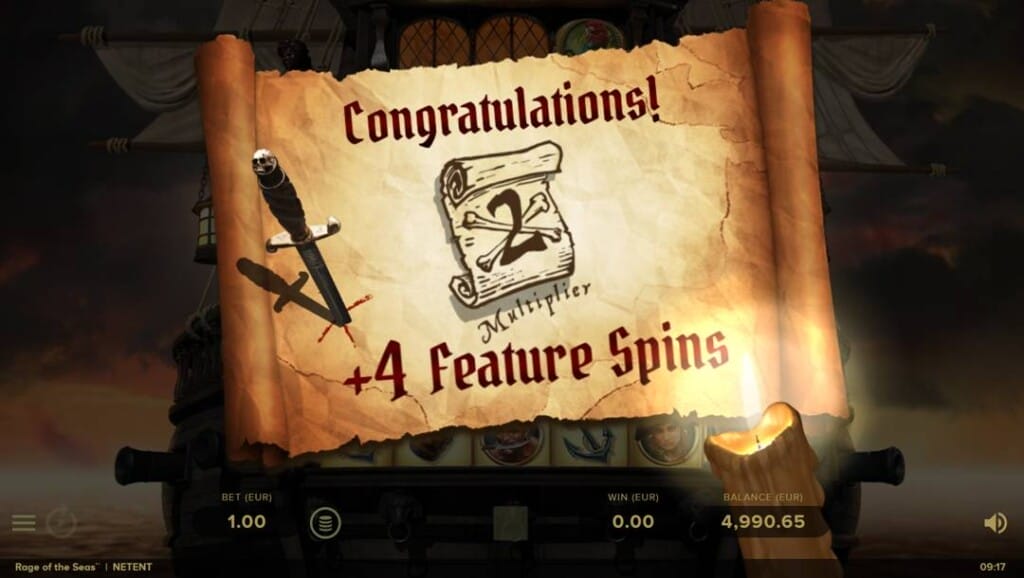A screenshot of the Rage of the Reels Feature Spins feature. A dramatic pirate ship dominates the background, with an aged parchment scroll with bold text reading “Congratulations! 2x Multiplier +4 Feature Spins” in the foreground. A lit candle at the bottom right casts a warm glow, illuminating the edge of the parchment and revealing a high balance at the bottom. 
