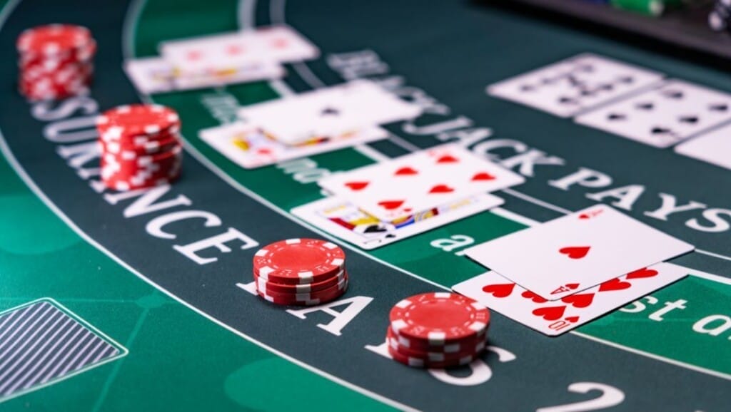 Close-up of a blackjack table showing red casino chips and multiple hands of playing cards in play.