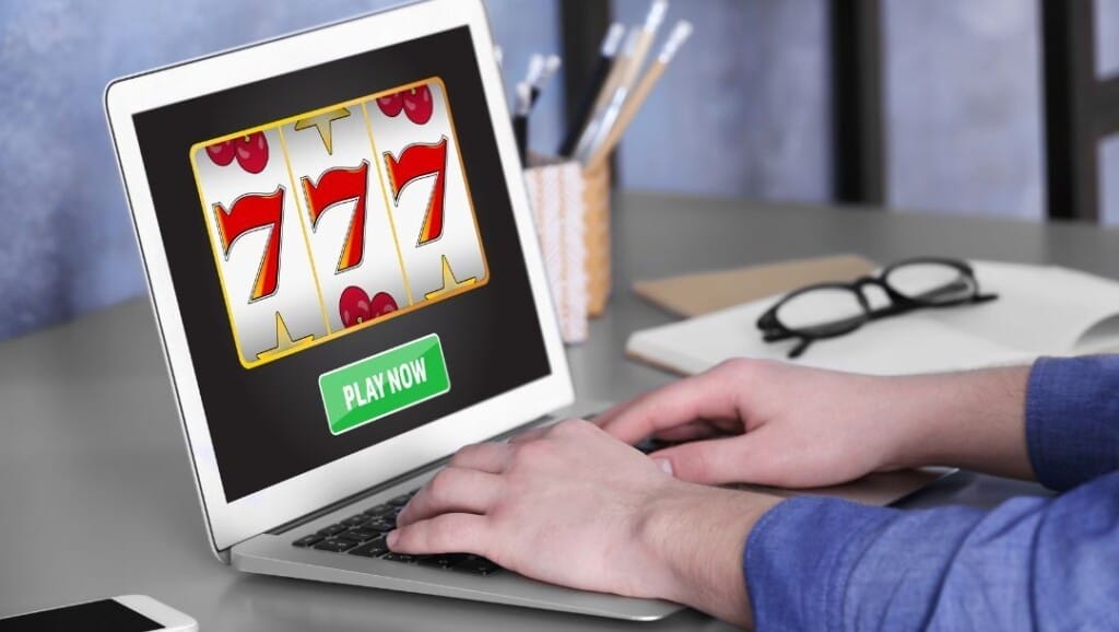 Orang yang memainkan permainan slot online di laptop yang menunjukkan tiga 7s dan tombol 