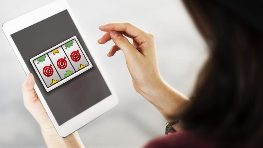 Woman playing a slot machine game on a tablet, showing three matching target symbols on the screen.