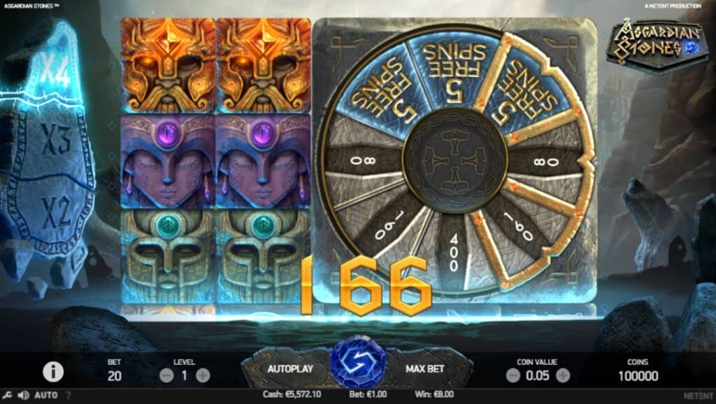 A screenshot of the slot reels in Asgardian Stones. The bonus wheel is activated, showing free spins and cash prizes. The 4x multiplier on the multiplier stone sculpture to the left of the reels is highlighted. The backdrop is a river running between two mountains.