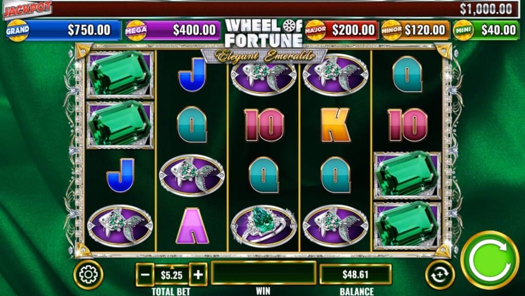 A screenshot of the Wheel of Fortune Elegant Emeralds slot reels. The background consists of luxurious emerald green fabric. The slot reels in the foreground feature a mix of emerald-themed and regular slot symbols.