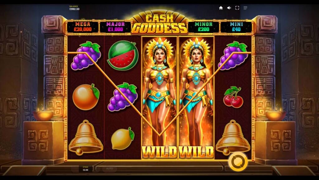 A screenshot of a wild symbol win in the Cash Goddess slot. The game is set inside a dimly lit stone Aztec temple. The slot reels are placed in the doorway of this temple and are filled with fruit slot symbols and two Aztec priestess symbols. Above the slot reels are the four jackpots.