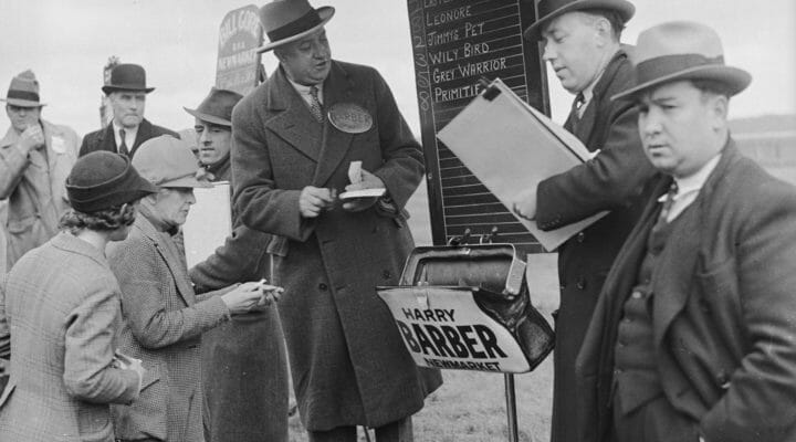 Two bookies taking bets on horse racing in 1936 with odds displayed on a blackboard