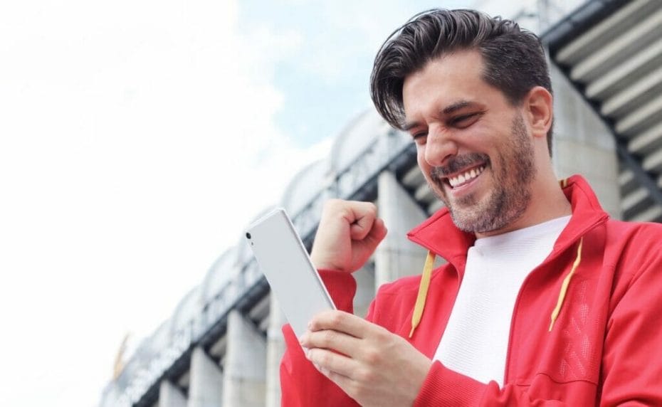 Man wearing red jacket holding smartphone celebrating online win