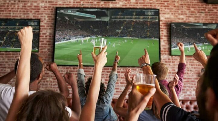 Rear view of fans watching a game in a sports bar on TV screens
