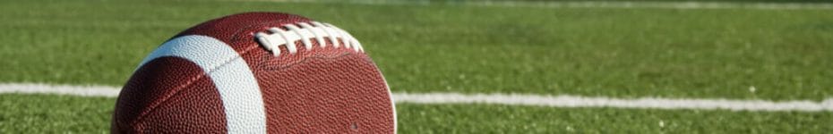 Closeup of an American football on field with goal post in background.