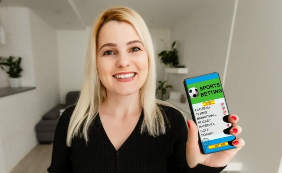 A woman holds up a mobile phone with a list of virtual sports for betting on screen.
