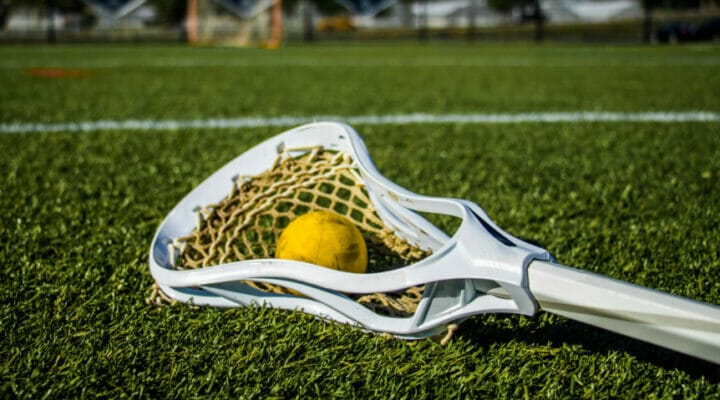 Yellow ball and lacrosse stick lying on a green playing field.