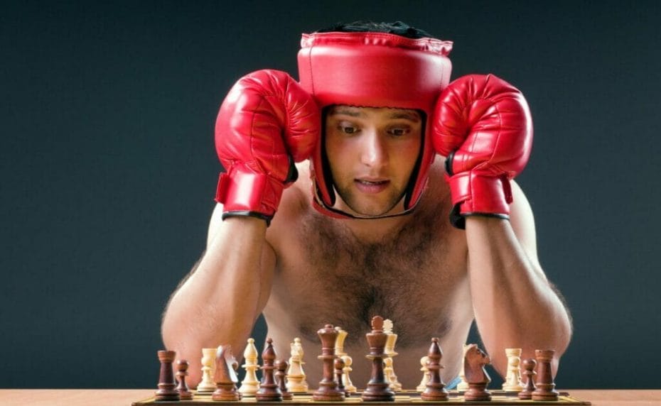 A man wearing boxing gear sits in front of a chess board, thinking about his move.