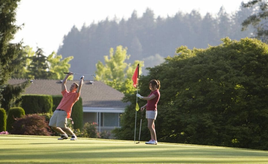 A woman holding the flag on the green while a man celebrates with his club and hands in the air