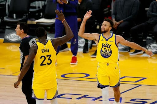 Stephen Curry high-fives Draymond Green on the basketball court.