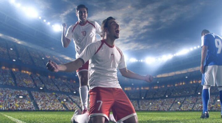 Two soccer players celebrate a win while a member of the opposition walks away.