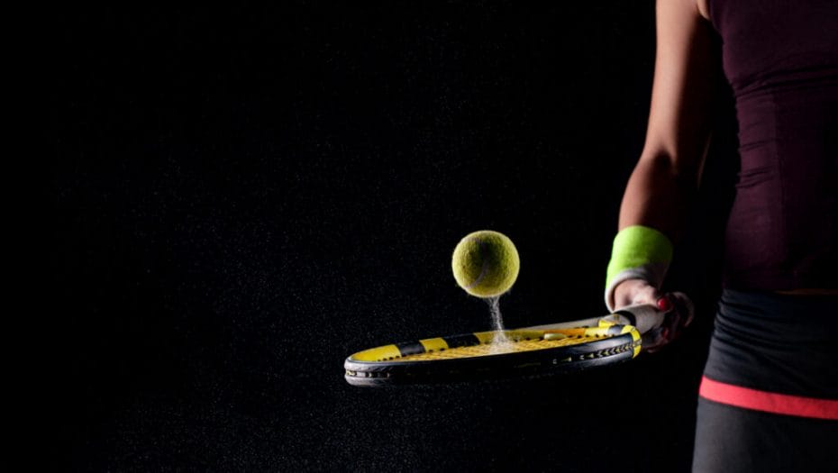 A woman bounces a ball of a tennis racquet on a black background.