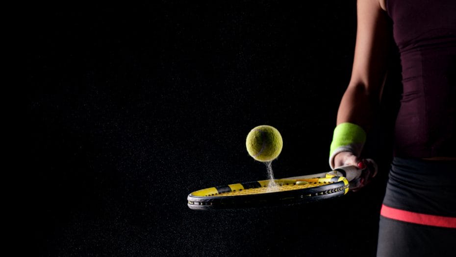 A woman bounces a ball of a tennis racquet on a black background.