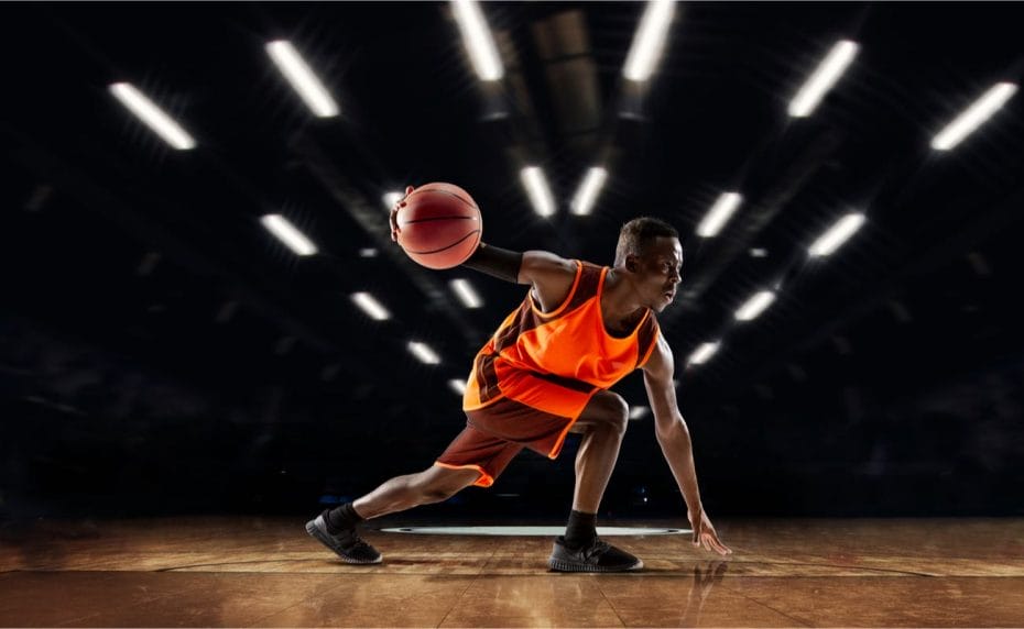 A basketball player in action with flashlights in the gym background.