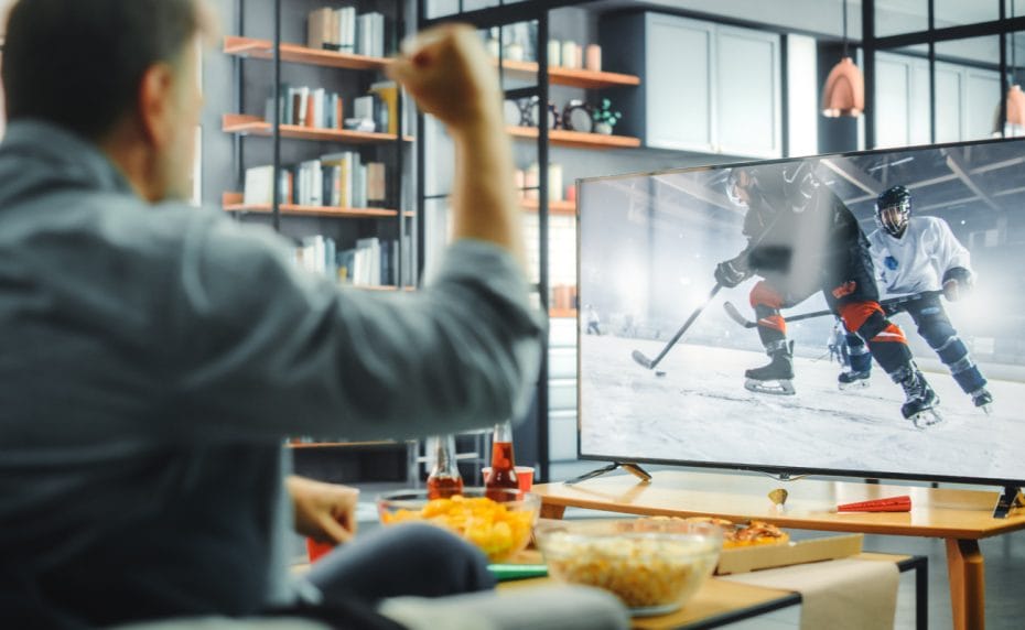 Person shaking his fist while watching an ice hockey game on TV.