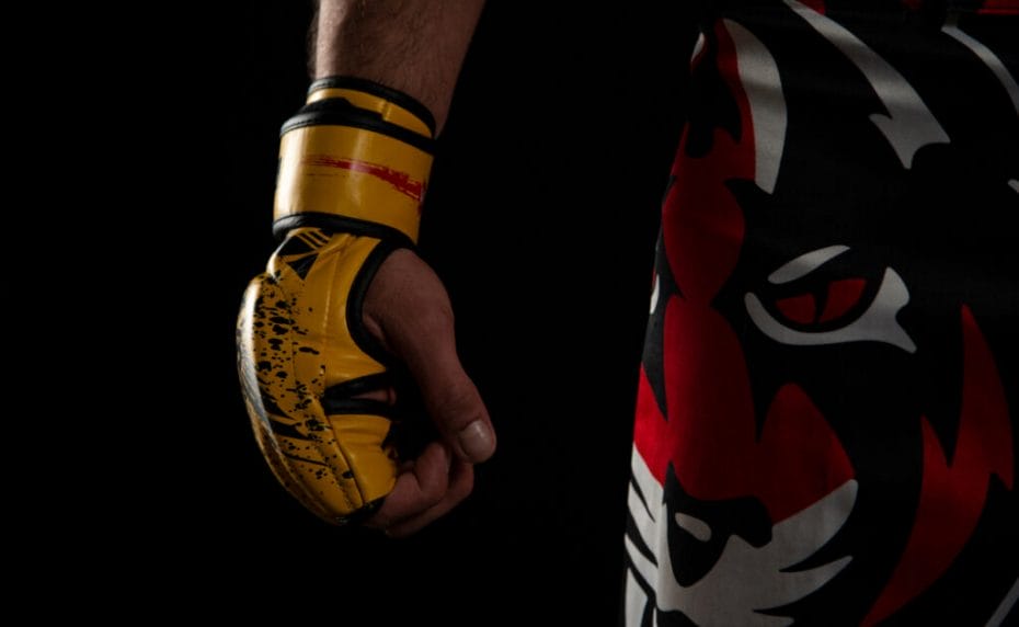 Mixed martial arts (MMA) fighter. Detail of the yellow glove with tiger pants on black background.