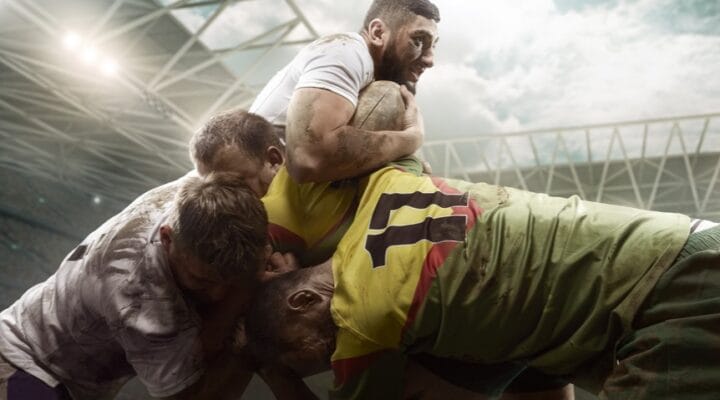 A player attempts to push through a tackle by two players with support from his teammate.