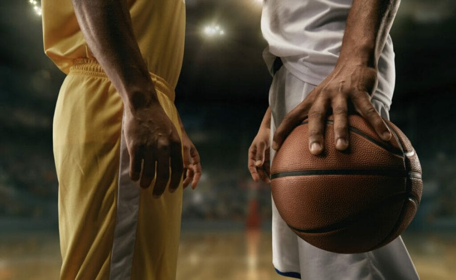 Seorang pemain bola basket berbaju kuning berhadapan dengan seorang pemain bola basket berbaju putih yang sedang memegang bola.