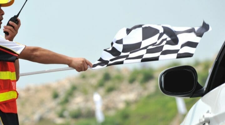 A man holds a racing flag by a car window.