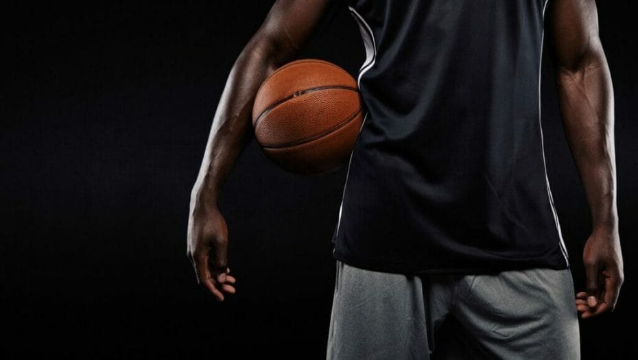 A basketball player stands with a basketball pinned to his side underneath his arm.