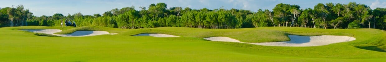 A golf cart and player next to bunkers on a golf course.