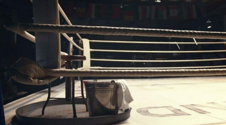 A stool and a bucket with a towel in the corner of a boxing ring.