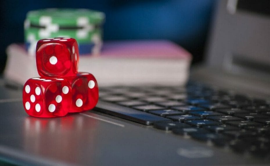 Red dice, playing cards and casino chips on a laptop.