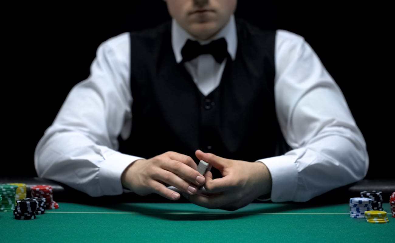 Professional croupier holding a pack of cards with stacks of poker chips on a green felt casino table. 